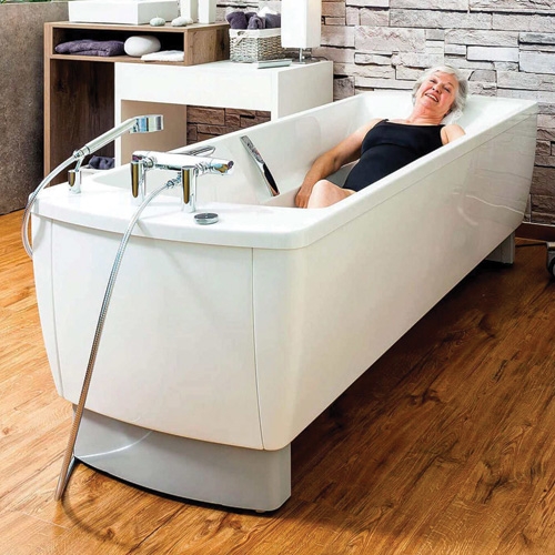 Osoba korzystająca z wanny rehabilitacyjnej Avero Comfort Fix w gabinecie kąpielowym na drewnianej podłodze.