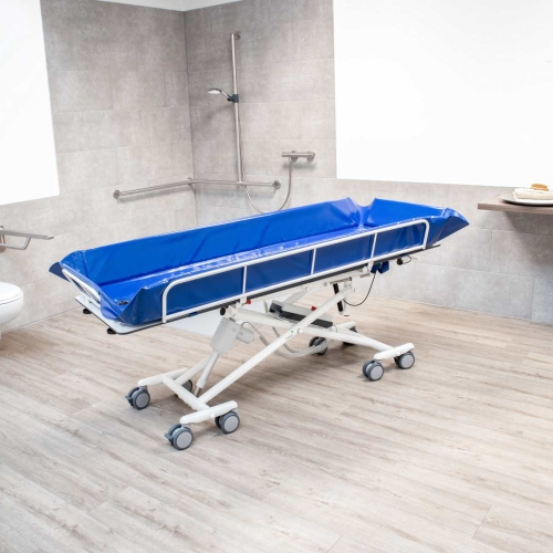 Wózek kąpielowy SINA w łazience przystosowanej do opieki z prysznicem i uchwytami ściennymi.